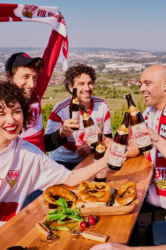 Eine Gruppe sitz an einer Bierbank und feiert mit Stuttgarter Hofbräu